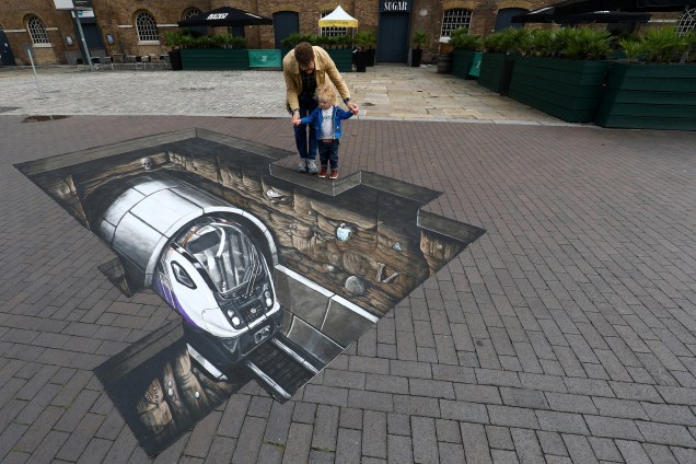 Um homem com uma criança observa de perto um desenho 3D feito perto do Museum of London Docklands, em Londres na Inglaterra - 03/08/2017