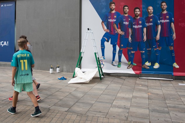 Menino vestindo camisa do Neymar passa por poster de jogadores do Barcelona, em frente ao Camp-Nou, na Espanha, que não mostra Neymar, após confirmação de que o jogador fechará contrato com o PSG - 02/08/2017