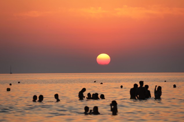 Banhistas nadam ao por do sol em Cava D'Aliga na ilha italiana da Sicília - 08/08/2017
