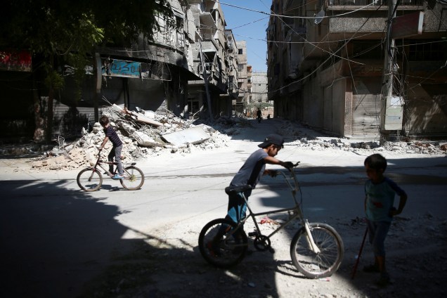Garotos andam de bicicleta em meio aos escombros de edifícios em Ain Tarma, subúrbio oriental de Damasco, Ghouta, na Síria - 23/08/2017