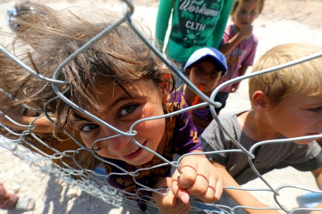 Crianças deslocadas da fortaleza síria do grupo Islâmico de Raqa, posam para uma foto atrás de uma cerca em um acampamento em Ain Issa - 23/08/2017