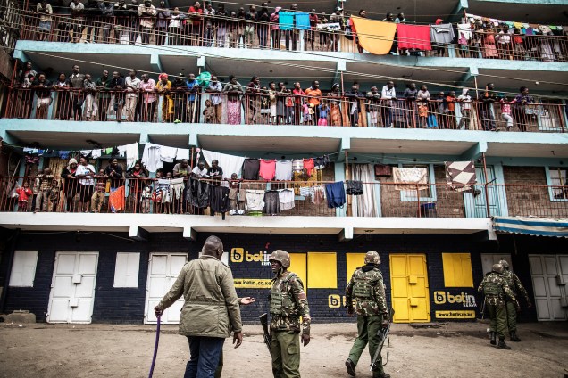 Moradores observam das sacadas enquanto policiais administrativos do Quênia patrulham a região da favela de Mathare, em Nairobi, durante o protesto contra o resultado das eleições gerais