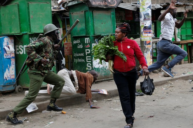Policiais tentam dispersar manifestantes durante protesto contra o resultado das eleições no Quênia, enquanto uma mulher passa com seus vegetais pelas ruas da favela de Mathare, em Nairobi