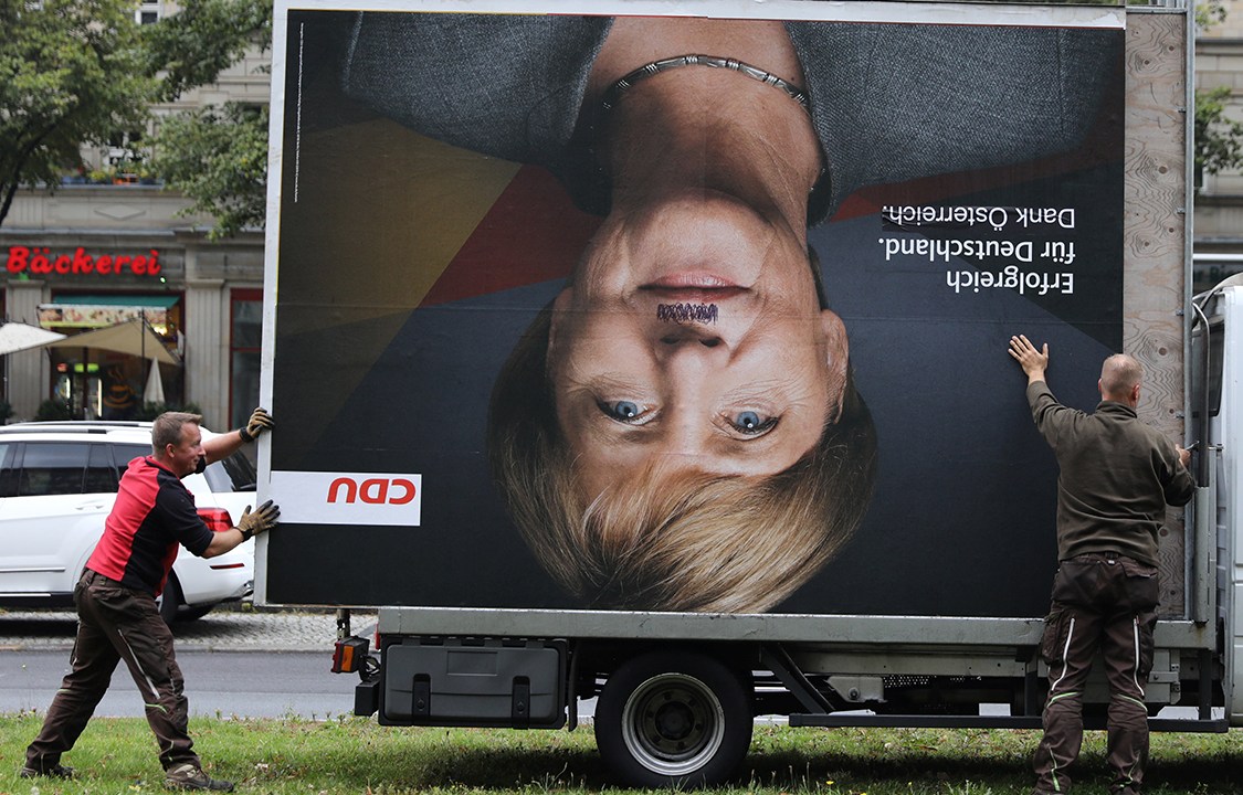 Funcionários removem outdoor de Angela Merkel após vândalos picharem o rosto da Chanceler, em Belim, Alemanha