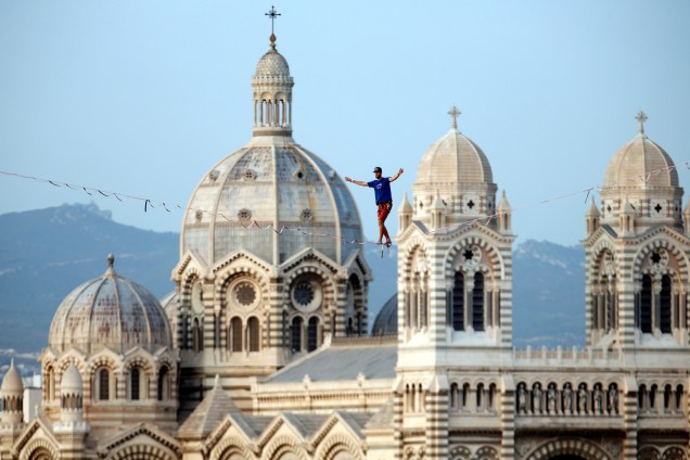 Sobre o Porto Velho de Marselha, na França, com a catedral principal da cidade ao fundo, um homem executa slackline durante um evento esportivo - 08/09/2017