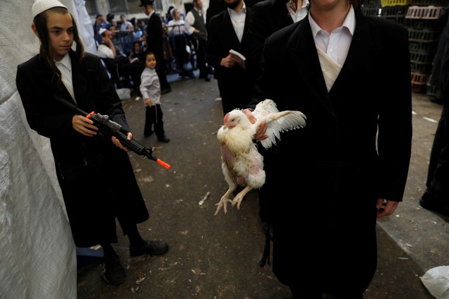 Um jovem judeu segura uma arma de brinquedo ao lado de um homem segurando uma galinha, durante o ritual de Kaparot, onde as galinhas brancas são abatidas como um gesto de expiação simbólica dos pecados, nas celebrações do Yom Kippur, o Dia judeu da expiação, no bairro Mea Shearim em Jerusalém - 27/09/2017