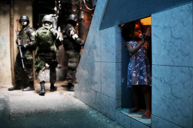 Uma garota é fotografada em uma porta sob uma escada enquanto ao seu redor policiais do Exército patrulham a Favela da Rocinha, durante operação no Rio de janeiro - 25/09/2017