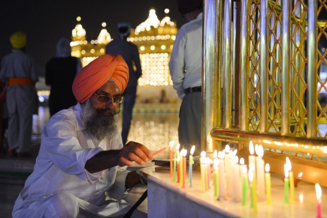 Um devoto sikhi é fotografado ascendendo velas enquanto os outros devotos se reúnem para as celebrações durante o Festival Diwali, no Templo Dourado, em Amritsar, na Índia - 18/10/2017