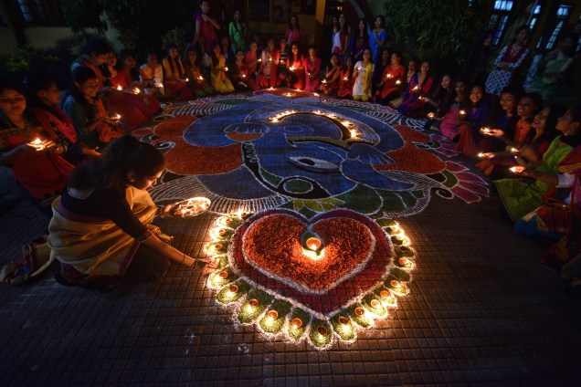 Estudantes fazem uma roda depois de acender as lâmpadas de óleo em torno de um "Rangoli", um desenho tradicional feito de pós coloridos e pétalas de flores, para as celebrações de Diwali, o festival hindu de luzes, em Guwahati, na Índia - 19/10/2017