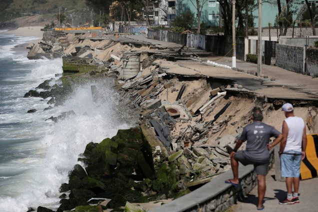 Dois homens olham uma erosão exposta ao longo do calçadão da praia da Macumba, no Rio de Janeiro, depois que uma tempestade no fim de semana fez com que ondas destruíssem a calçada - 17/10/2017