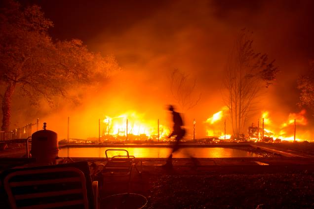 Um bombeiro caminha ao lado de uma piscina enquanto a casa ao lado é vista em chamas durante um incêndio florestal na região vinícola de Napa, na Califórnia, Estados Unidos - 09/10/2017