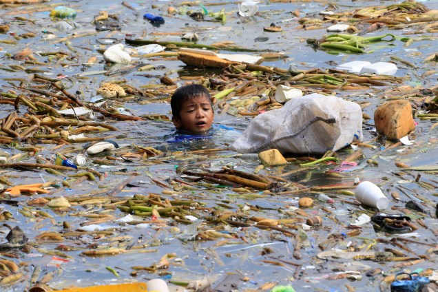 Menino coleta garrafas de plástico recicláveis em meio ao lixo ao longo da costa da Baía de Manila, na área das favelas de Baseco Filipinas - 16/10/2017
