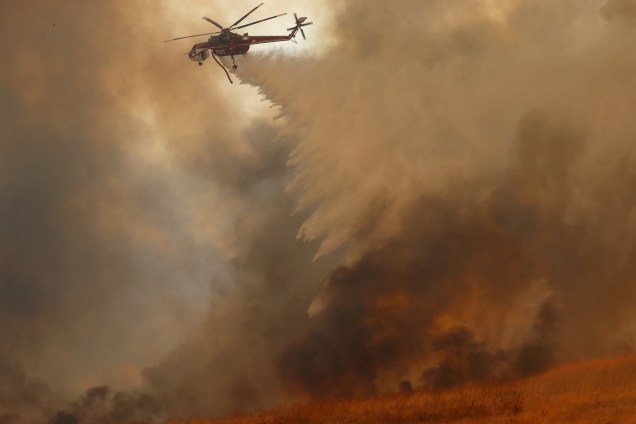 Um helicóptero do corpo de bombeiros derrama água na tentativa de conter o incêndio florestal que atingiu a cidade de Orange, no estado norte-americano da Califórnia - 09/10/2017