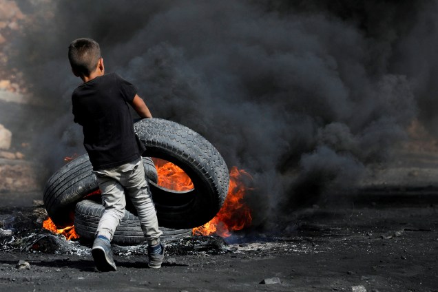 Um menino palestino coloca um pneu em chamas durante um confronto com tropas israelenses perto do assentamento judaico de Qadomem, na aldeia de Kofr Qadom, perto de Nablus, no território da Palestina - 20/10/207