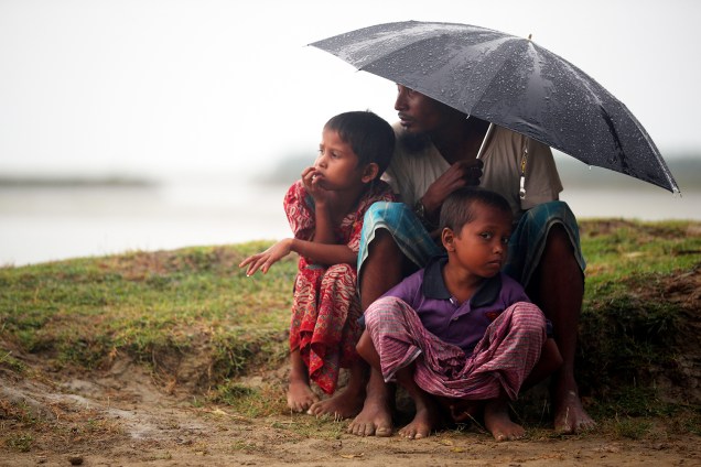 Refugiados se protegem da chuva enquanto aguardam permissão do Exército para prosseguirem viagem, em Teknaf, região de Bangladesh - 31/10/2017