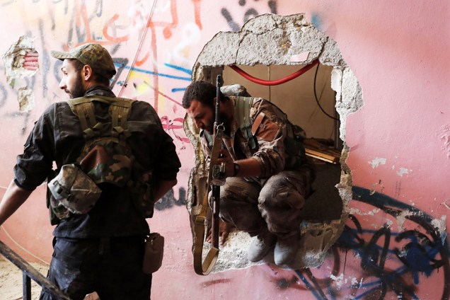 Soldados das Forças Democráticas Sírias passam por um buraco na parede enquanto se posicionam para combater militantes do Estado Islâmico, em Raqqa - 04/10/2017