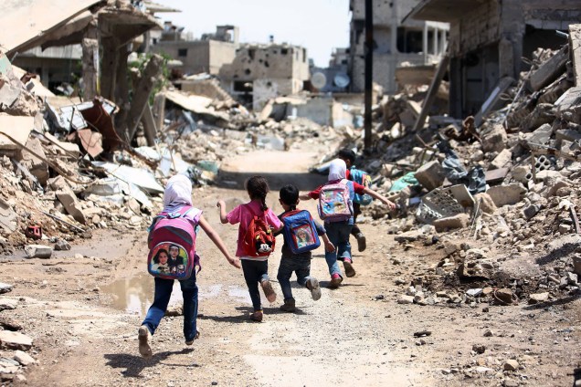 Crianças caminham entre escombros de edifícios destruídos por bombardeios, em área controlada por rebeldes na cidade de Damasco, Síria