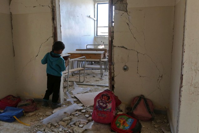 Criança observa sala de aula parcialmente destruída por um ataque aéreo, em uma escola na cidade de Utaya, Síria - 07/03/2017