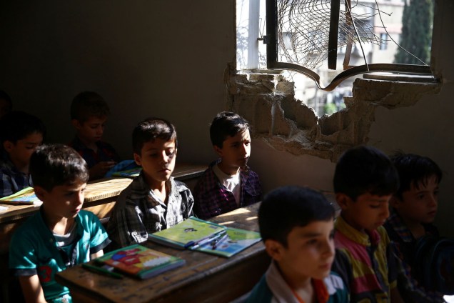Crianças estudam próximo à janela destruída, no primeiro dia de aula, em uma escola na cidade de Douma, Síria