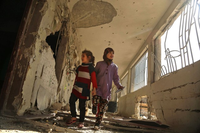 Crianças sírias caminham em escola destruída na cidade sitiada de Saqba, um dia após ataques aéreos do governo - 09/11/2017