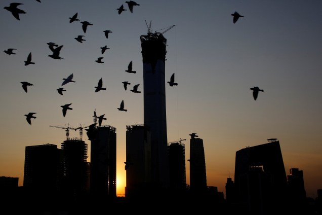 Pombos são fotografados sobrevoando o Distrito Central de Negócios, enquanto o sol se põe atrás do prédio da CITIC no centro de Pequim, na China - 15/11/2017