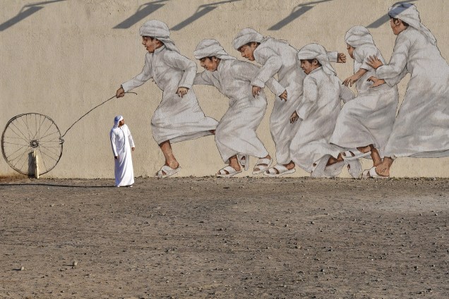 Homem atravessa um mural gigante retratando meninos correndo atrás de uma roda, em Dubai nos Emirados Árabes - 30/11/2017
