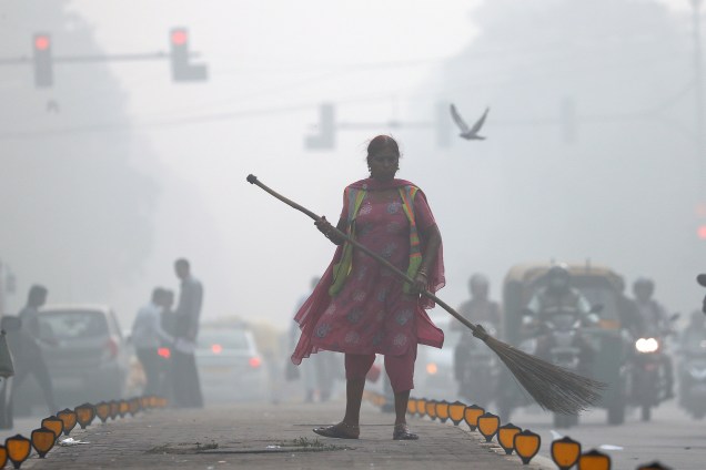 Mulher varre a rua em meio à densa camada de poluição no trânsito da cidade de Deli, na Índia - 10/11/2017