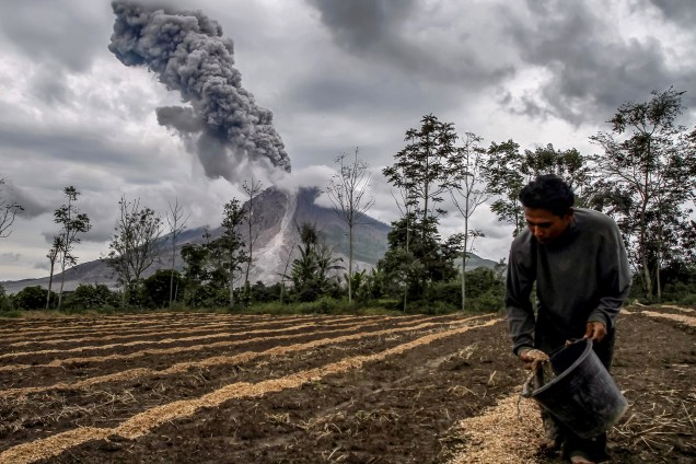 Agricultor fertiliza sua terra enquanto o vulcão Monte Sinabung entra em erupção, em imagem feita a partir de Karo, na Indonésia. O Monte Sinabung voltou à ativa em 2010 pela primeira vez depois de 400 anos - 14/11/2017