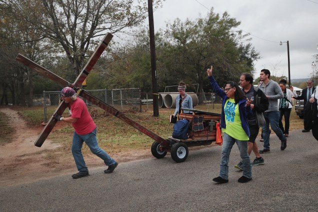 Stephen Hope carega uma cruz pela cidade seguido de outros fiéis após o culto dominical da Igreja Batista de Sutherland Springs, no Texas. A cerimônia foi realizada em uma barraca em um campo de beisebol da cidade - 12/11/2017