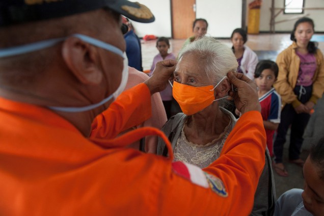 Oficial da agência de gerenciamento de desastres BPBD coloca uma máscara em uma mulher idosa em um abrigo para residentes que tiveram que deixar suas casas devido à erupção do vulcão Monte Agung em Bali, na Indonésia - 27/11/2017