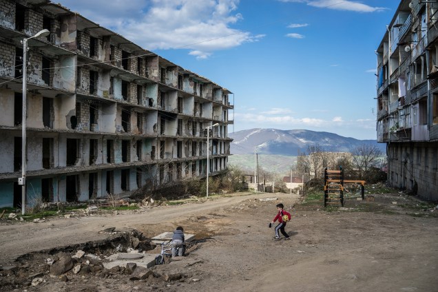 Crianças brincam próximo a um prédio destruído pela guerra, em Artsakh.