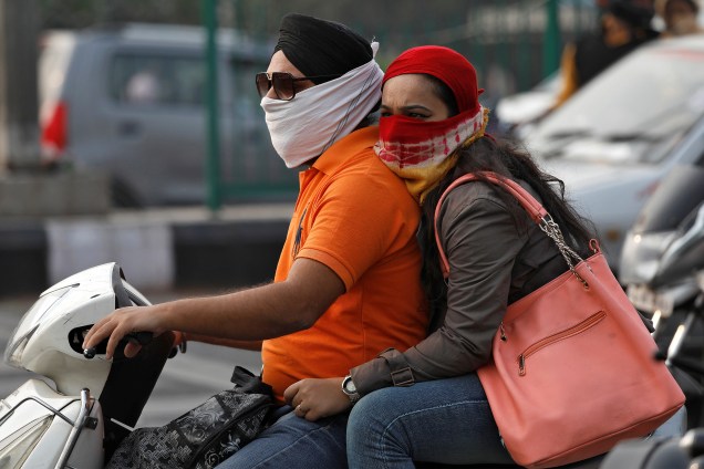 Um homem e uma mulher são vistos com lenços cobrindo as vias aéreas para evitar o ar poluído enquanto andam de moto em Nova Deli, capital da Índia - 16/11/2017