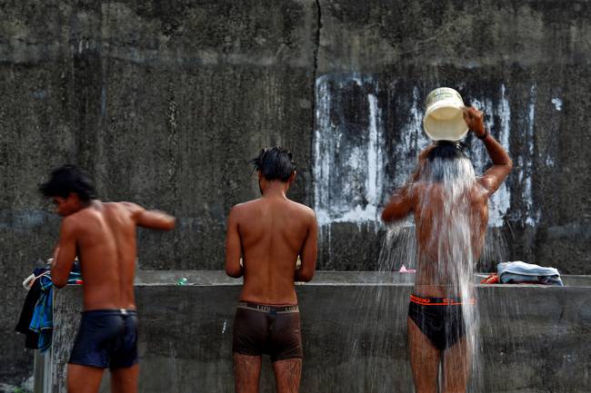 Trabalhadores tomam banho com um balde no centro de Mumbai, na Índia
