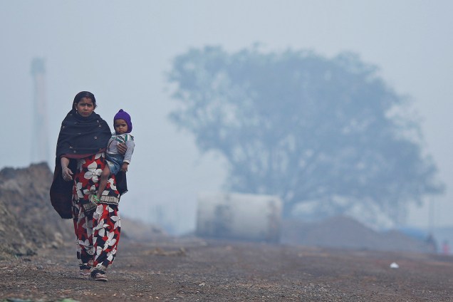 Mulher carrega filho do colo e caminha por uma estrada em Nova Délhi, na Índia - 20/12/2017
