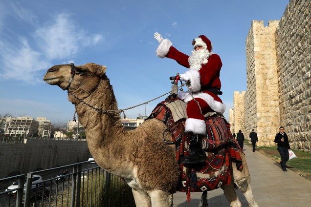 Papai Noel fantasiado cumprimenta crianças enquanto monta em um camelo, no centro de ditribuições de árvores de natal na cidade velha de Jerusalém - 21/12/2017