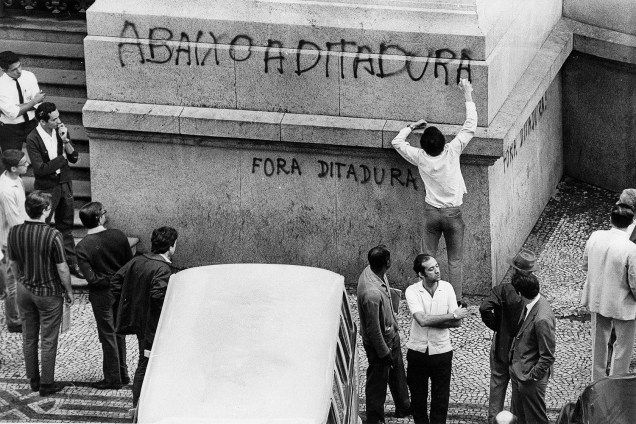 Estudante pichando fachada de prédio com os dizeres "Abaixo a Ditadura".