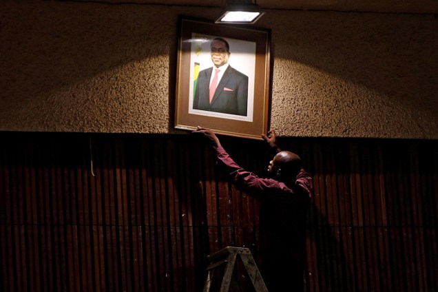 Funcionário coloca retrato do presidente do Zimbábue, Emmerson Mnangagwa, antes = de uma reunião do comitê central do ZANU-PF no centro de Harare, no Zimbábue