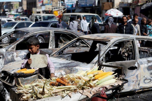 Garoto vende milho grelhado perto de carros danificados durante confrontos recentes entre homens Houthi e forças leais ao ex-presidente do Iêmen, Ali Abdullah Saleh, em Sanaa, Iêmen - 05/12/2017