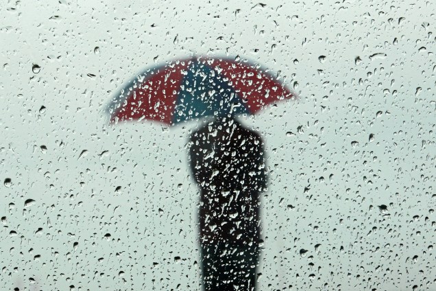 A silhueta de um homem carregando um guarda-chuva é vista através de uma janela molhada pela chuva na cidade de Colombo, no Sri Lanka - 01/12/2017