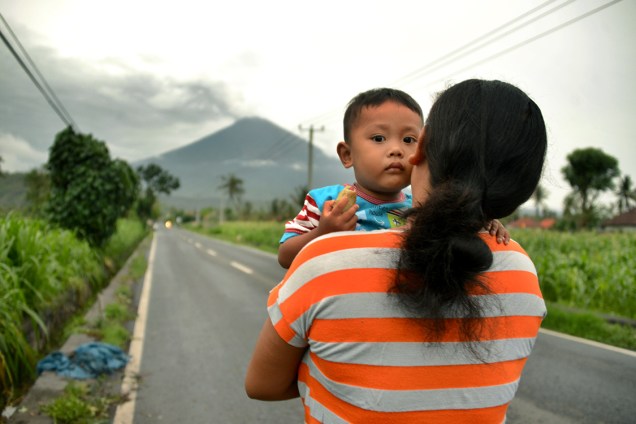 Mulher carrega seu bebê em estrada com vista para o vulcão Agung, em Bali, na Indonésia