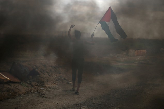 Manifestante segura uma bandeira palestina durante confronto com tropas israelenses em um protesto contra a decisão dos Estados Unidos de reconhecer Jerusalém como a capital de Israel