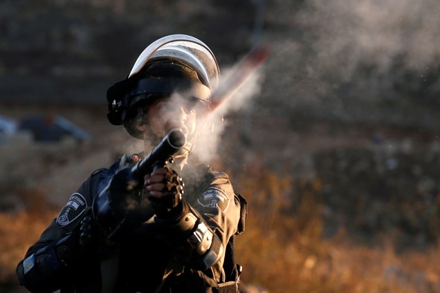 Um policial israelense de fronteira atira bombas de gás contra manifestantes palestinos, em Ramallah - 08/12/201