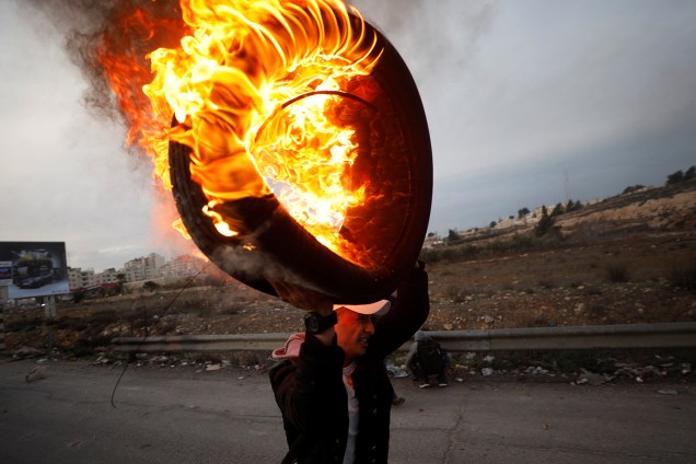 Palestino carrega pneu em chamas durante confronto com tropas israelenses, em protesto realizado contra a decisão do presidente dos Estados Unidos, Donald Trump, de reconhecer Jerusalém como a capital de Israel - 10/12/2017