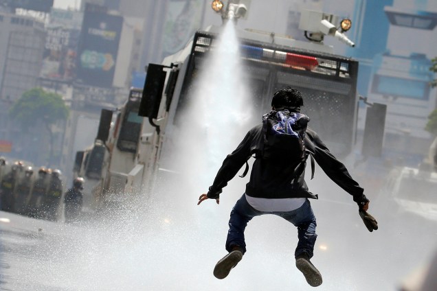 Manifestante salta para escapar de jatos d'água lançados por tropas do governo venezuelano, durante protestos contra o presidente Nicolás Maduro, em Caracas - 26/05/2017