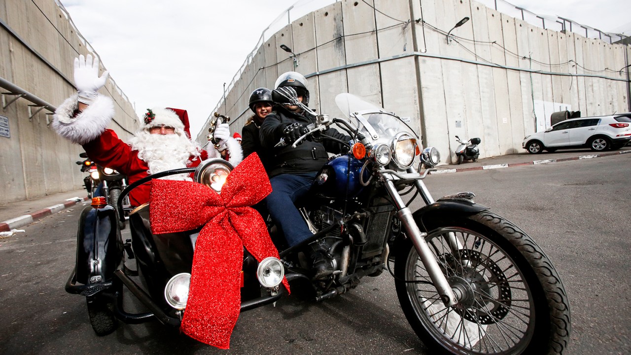 Homem vestido de Papai Noel acena para pedestres em uma motocicleta, na cidade de Belém, localizada na Cisjordânia - 24/12/2017