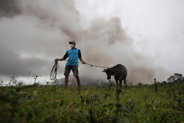 Fazendeiro resgata seu bezerro para levá-lo ao centro de evacuações, após o vulcão Mayon expelir cinzas em Camalig, província de Albay, nas Filipinas - 17/01/2018
