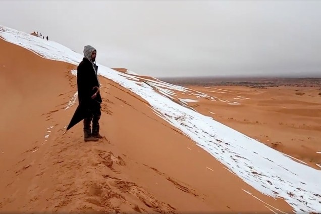 Homem olha para uma duna de areia coberta de neve no Deserto do Saara, em Ain Sefra, na Argélia - 07/01/2018