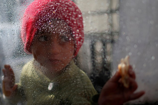 Uma menina palestina olha através de um vidro marcado com pingos de chuva fora da casa de sua família, no campo de refugiados de Al-Shati, na cidade de Gaza - 17/01/2018