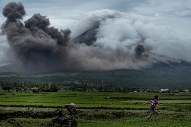 Menino brinca enquanto ao fundo enormes nuvens de cinzas cobrem o vulcão Mayon durante uma erupção em Camalig, nas Filipinas - 18/01/2018