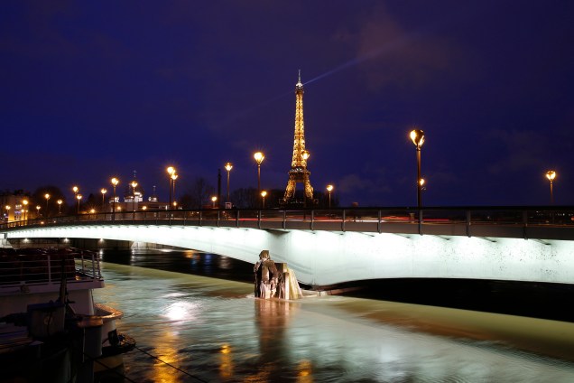 Torre Eiffel iluminada, ao lado do rio Sena, com níveis de água elevados cobrindo a estátua Zouave na ponte Pont d'Alma, em Paris - 25/01/2018